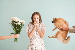 People giving flowers and dog to young woman suffering from allergy on light background