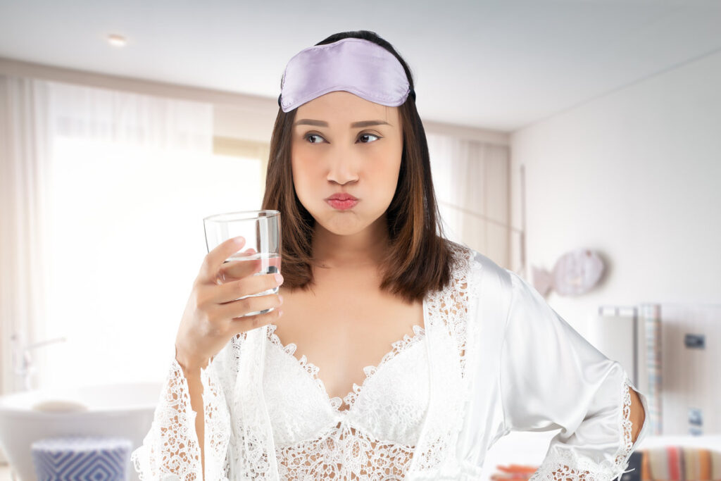 Asian woman rinsing your mouth with water after brushing after waking up. Dental health concepts. Lady in satin nightwear wearing white lace robe standing gargle on bathroom in the morning