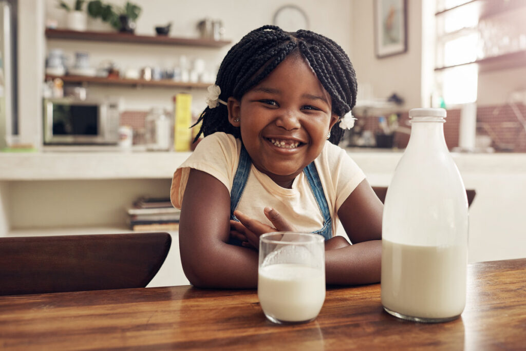 Children, portrait and African girl with milk in kitchen for strong teeth, bones and gut health balance. Face, smile and kid at home with glass bottle dairy drink for vitamin D, calcium or benefits.