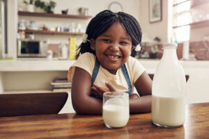 Children, portrait and African girl with milk in kitchen for strong teeth, bones and gut health balance. Face, smile and kid at home with glass bottle dairy drink for vitamin D, calcium or benefits.