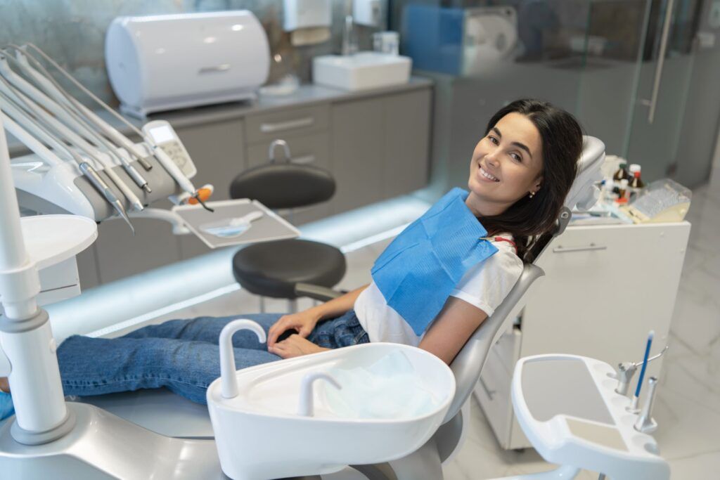 Pretty brunette happy female patient sitting in the chair at dental clinic.